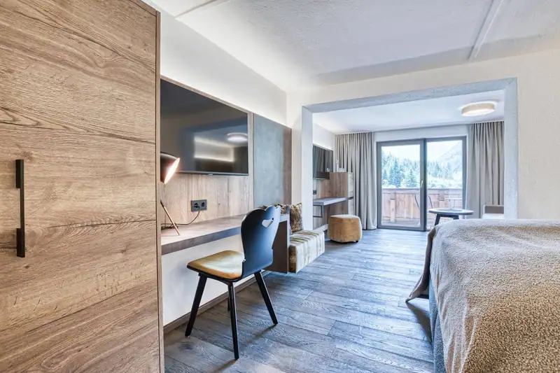 View through the suite: desk, TV, bench seat and living area with balcony door and mountain view
