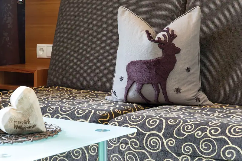 Cushion with deer motif on the sofa bed, in front of it a wooden heart saying “Herzlich Willkommen” (welcome)