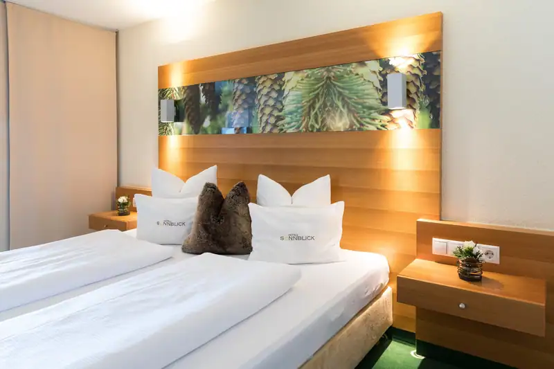 Bed with cushions with the Sonnblick logo in front of the illuminated wooden headboard