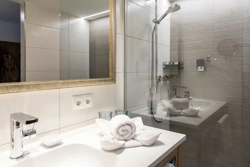 Washbasin with mirror and towels, next to it the shower with glass wall