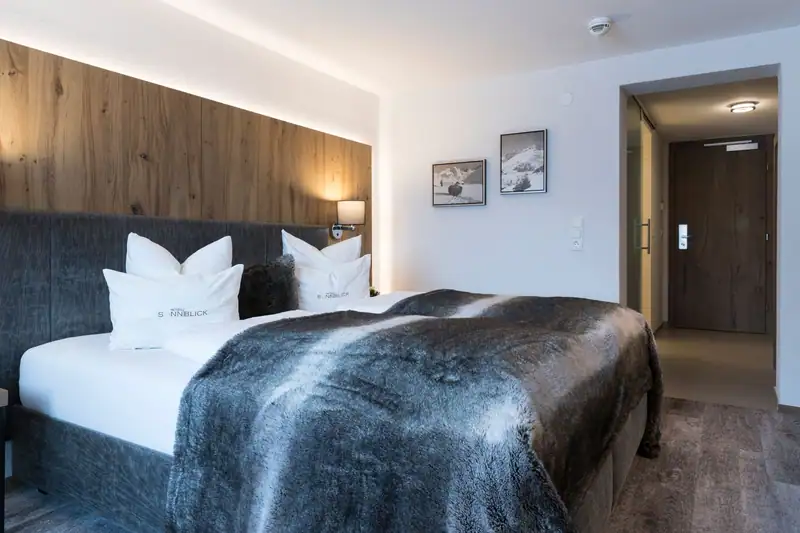 Box-spring bed with fur throw, mountain photographs and entrance area behind