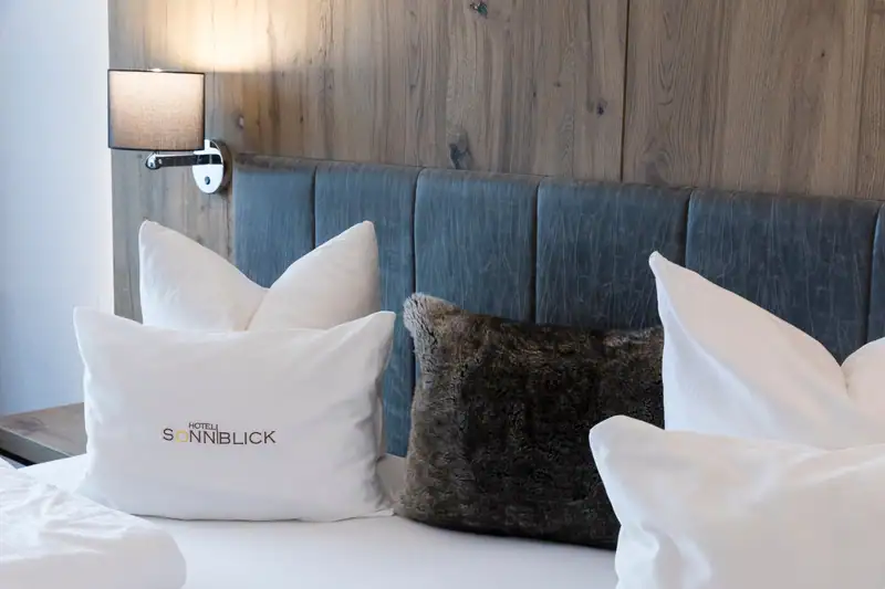 Cushion with the Sonnblick logo in front of the upholstered headboard and reading lamp