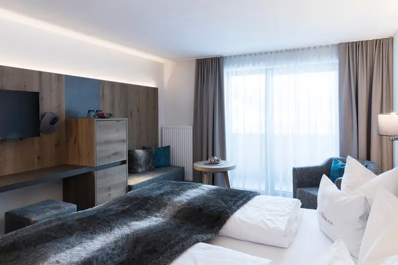 View across the bed to the TV, desk, bench seat, armchair and balcony door