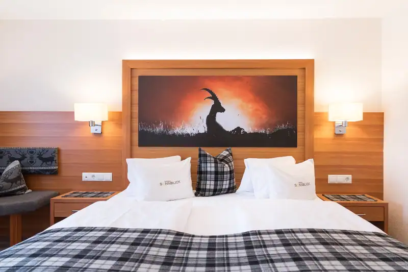 Double bed from the front with reading lamps and ibex picture in a wooden frame