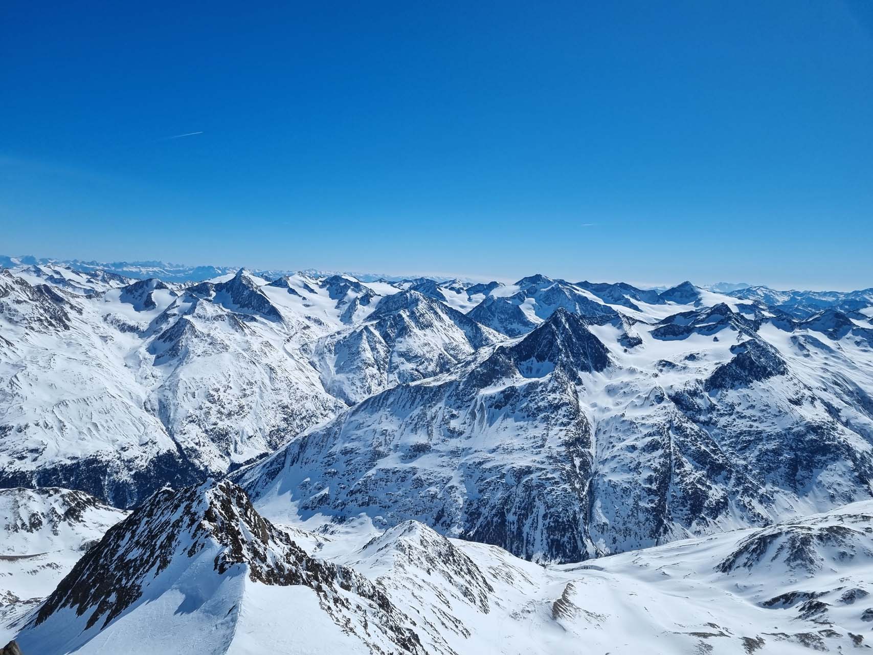 Successful ski tourers stand at the summit cross of the Wildspitze (3,770 m) in the Pitztal valley and enjoy the panoramic view over the Ötztal Alps.